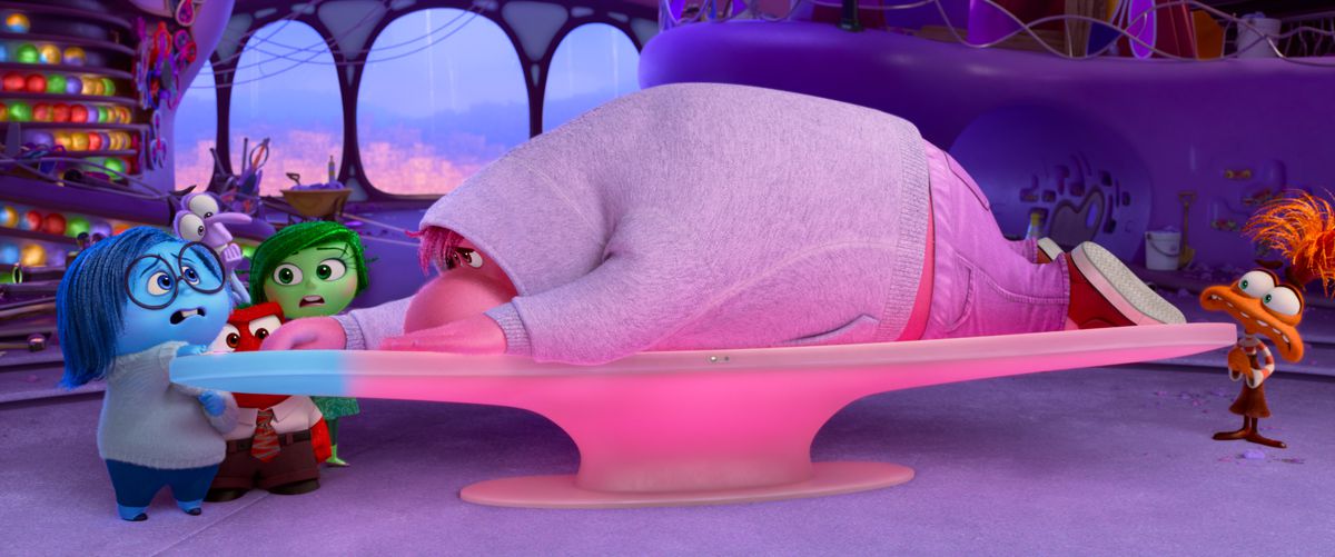 Embarrassment, a large, blobby, pink fellow in a grey hoodie, lies sprawled across the control board in emotions HQ as the other characters stand around looking worried in Pixar Animation Studios’ Inside Out 2