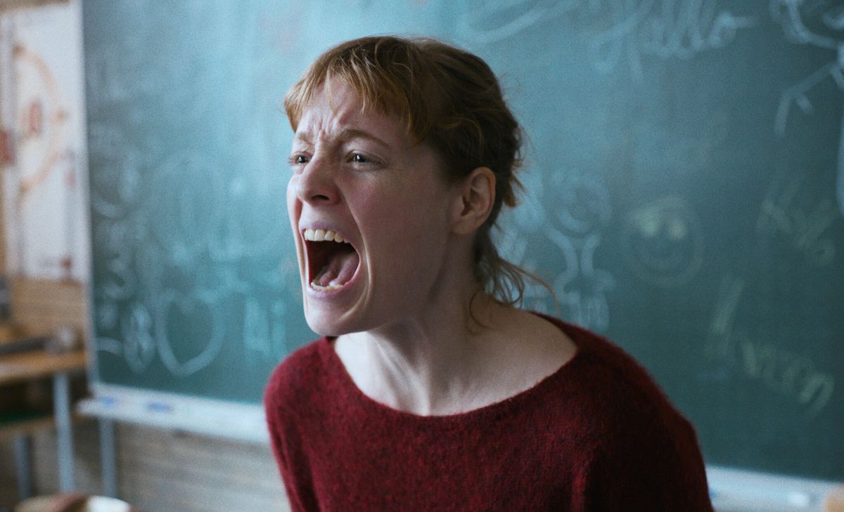 A woman in a red sweater screaming in front of a chalkboard in The Teacher’s Lounge.