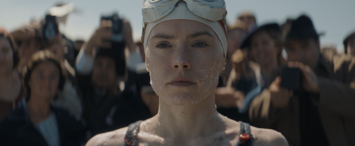 A close-up of a woman wearing swimming goggles surrounded by photographer with cameras in Young Woman and the Sea.