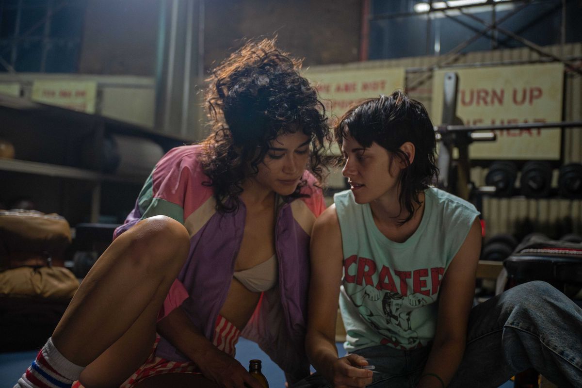 Two women sitting next to one another holding beer bottles in a boxing ring.