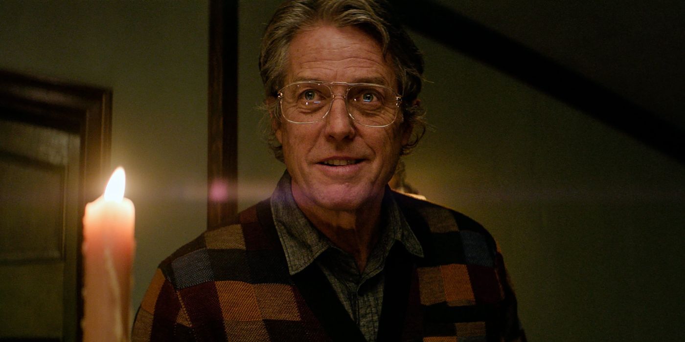 hugh grant with big glasses and a sweater lit by a candle in Heretic