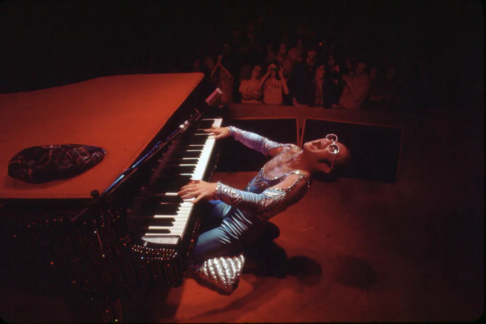 Archival photo of Elton John playing the piano in front of an audience