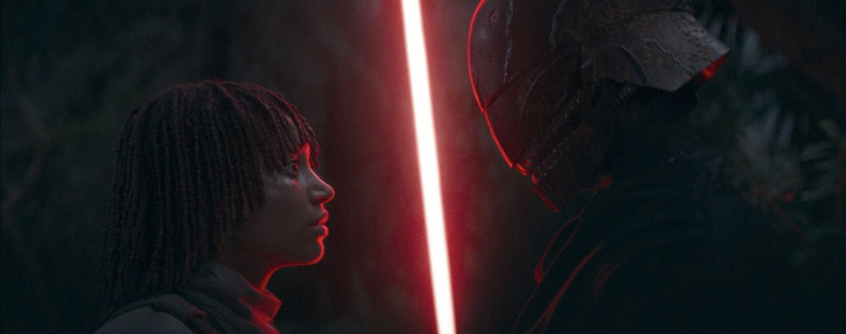 Mae (Amandla Stenberg) standing and looking at the Master up close, with a red light saber between them