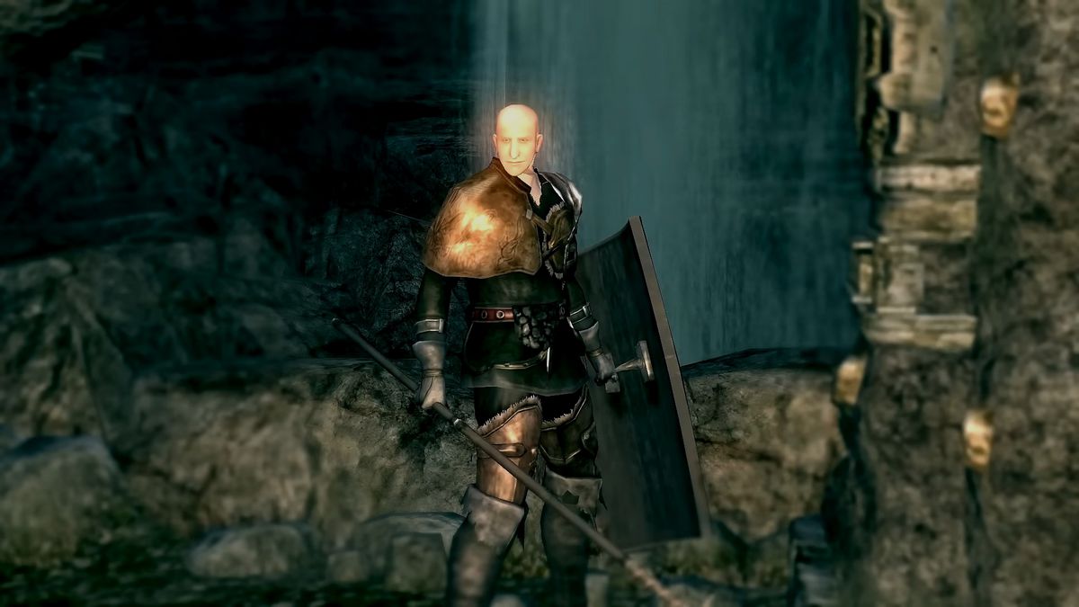 Patches stands next to a bridge lever, with spear and shield in h and, in a screenshot from Dark Souls Remastered